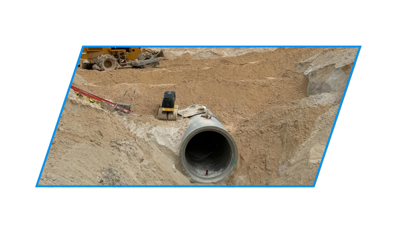 A large concrete pipe being installed in a sandy construction site with machinery in the background.