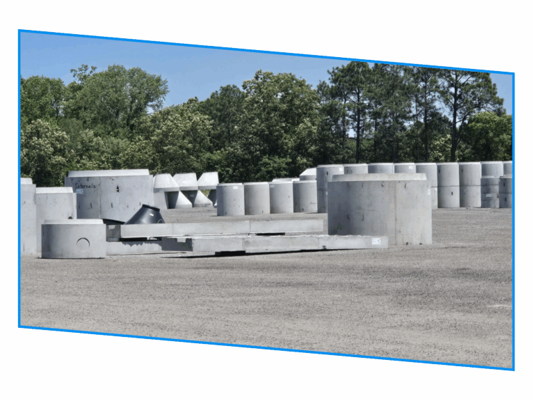Large concrete pipes and structures arranged outdoors on a gravel lot, with trees in the background.